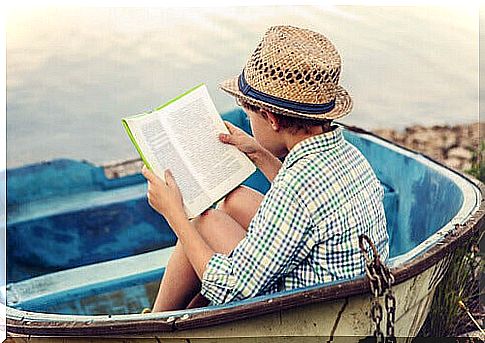 Child reading a book in a boat on the beach