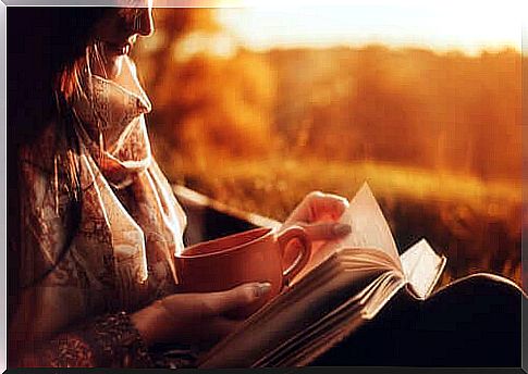 A woman reads a book and holds a cup